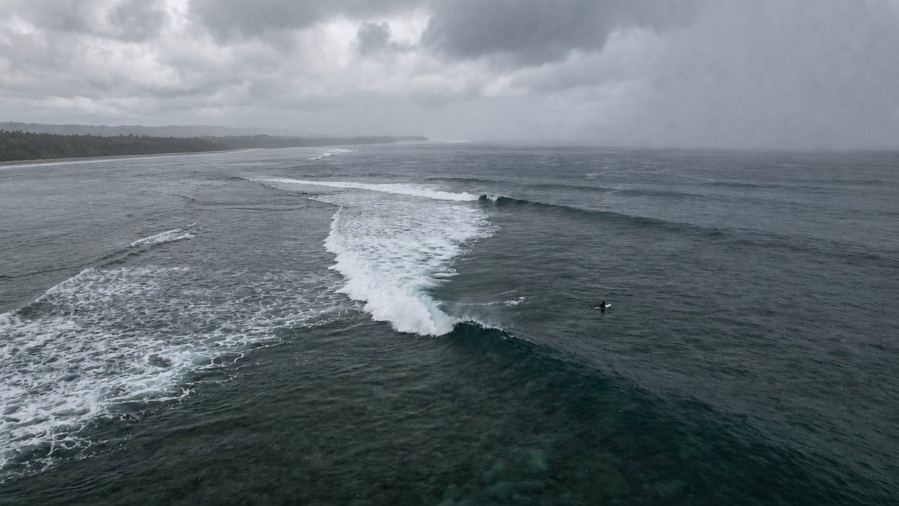 Aerial view of one surfer alone on a Philippine reef under heavy monsoon overcast as a swell line peels